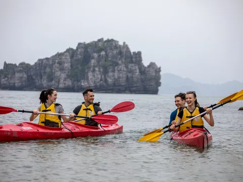 Four people in yellow life jackets kayaking in red and pink kayaks with dramatic limestone karst formations in the background.