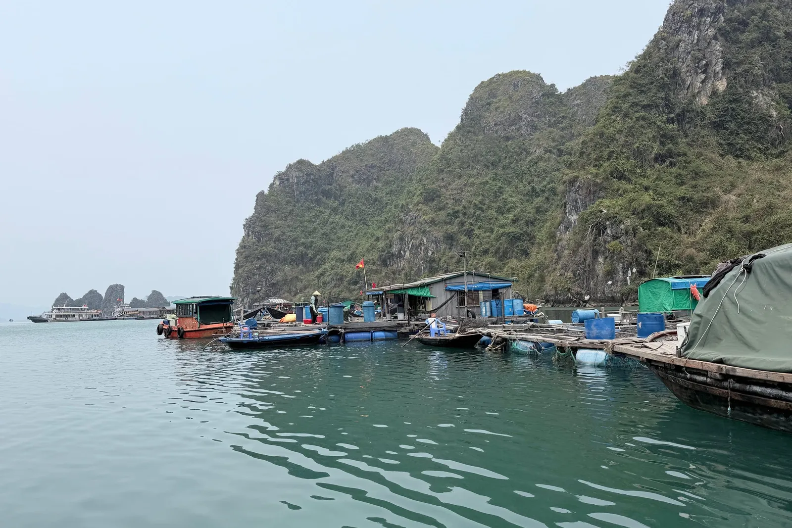 A floating village with houses and boats on green water surrounded by limestone karst mountains.
