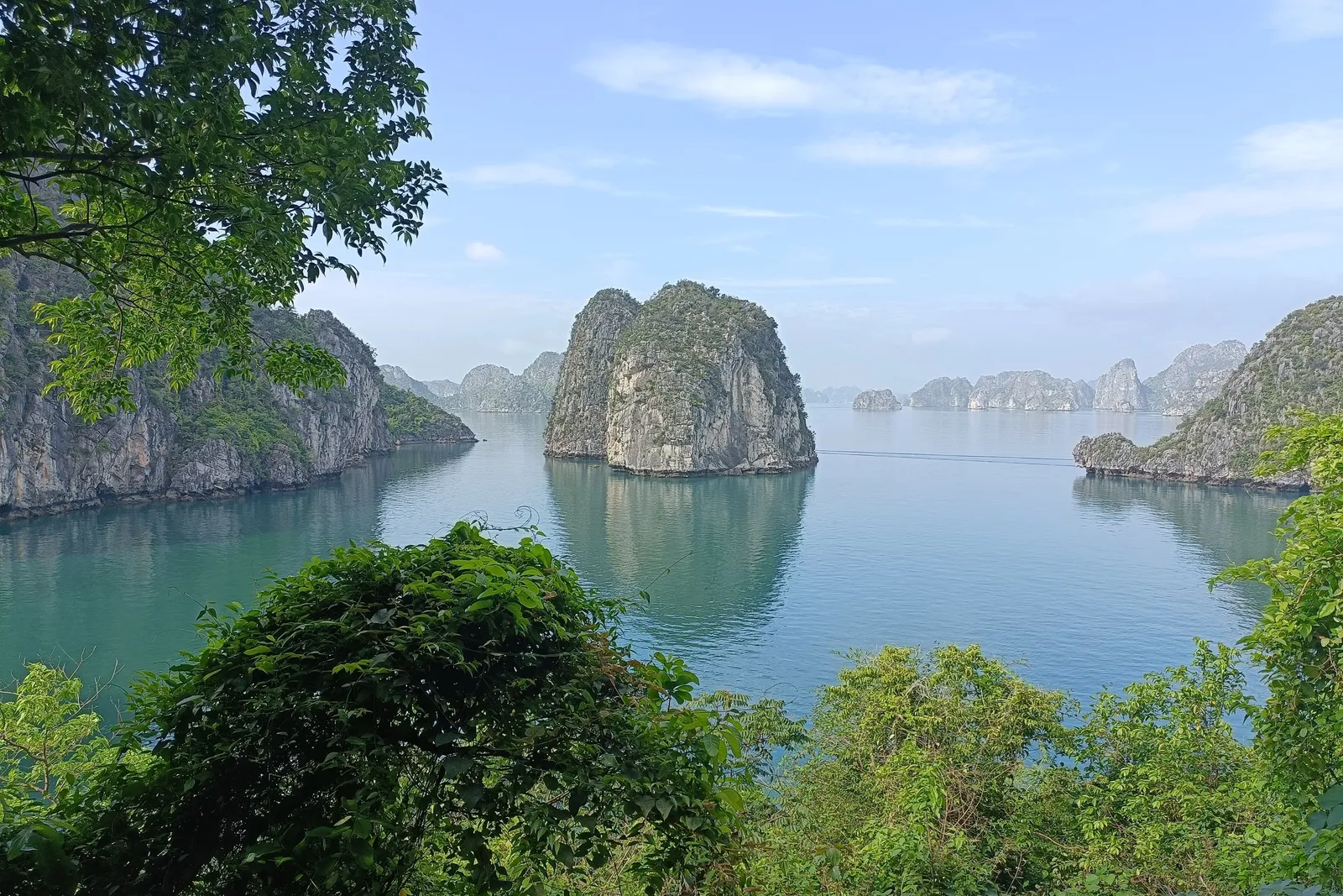 Limestone karst islands rising from calm turquoise water, framed by green foliage in the foreground.