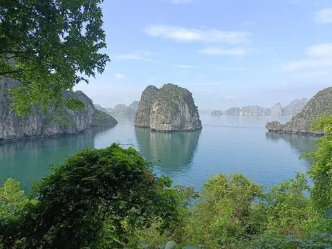 Limestone karst islands rising from calm turquoise water, framed by green foliage in the foreground.