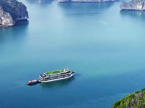 Elevated view of a multi-deck cruise boat with a small red tender anchored in turquoise water surrounded by forested limestone karst islands.