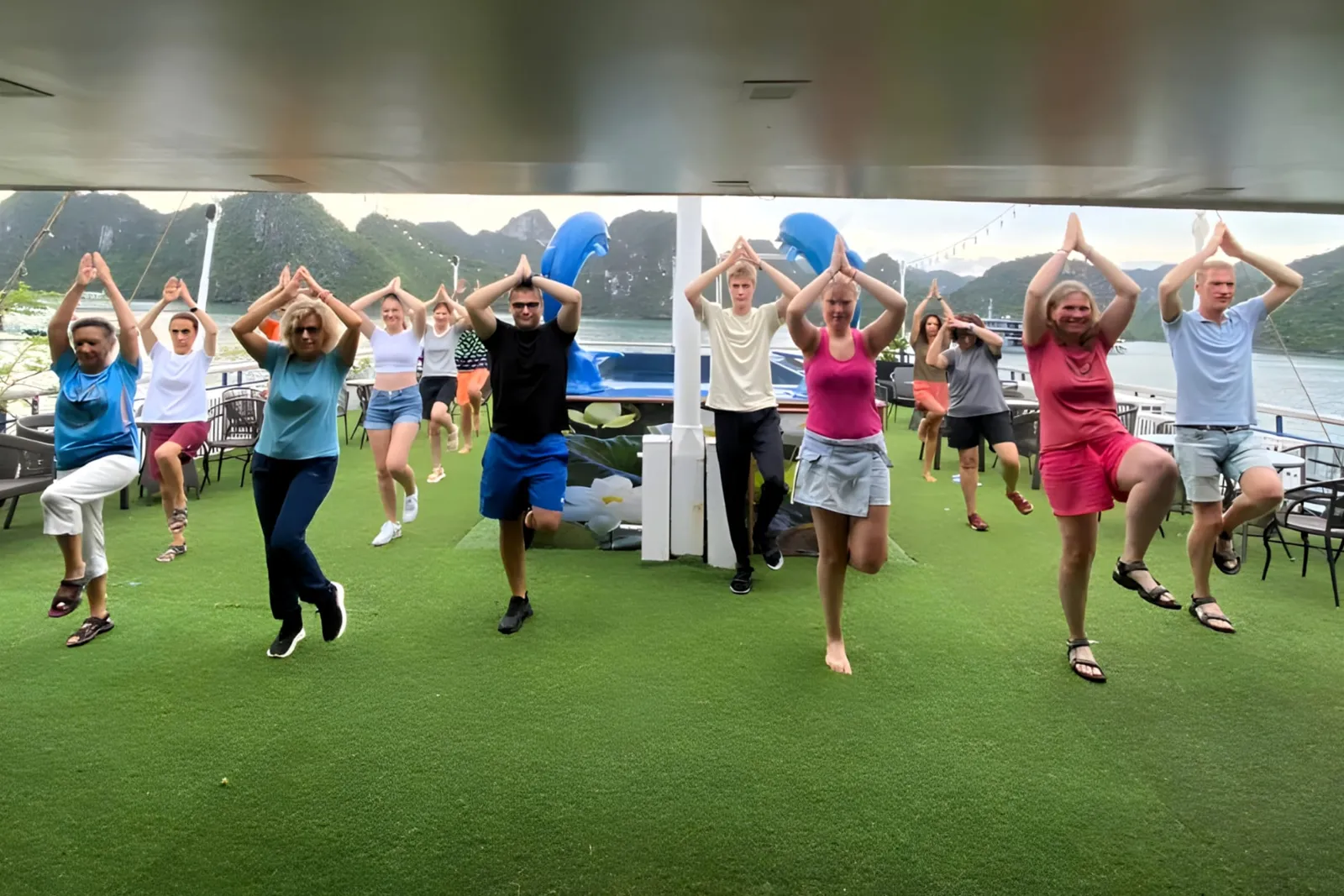 A group doing tai chi poses on the green-turf deck with the bay behind.