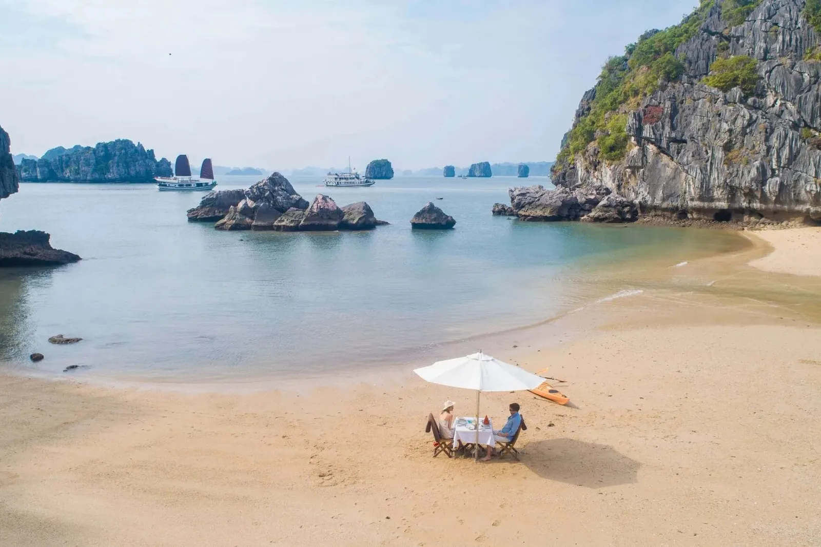 A small table with an umbrella on a sandy beach between limestone outcrops.