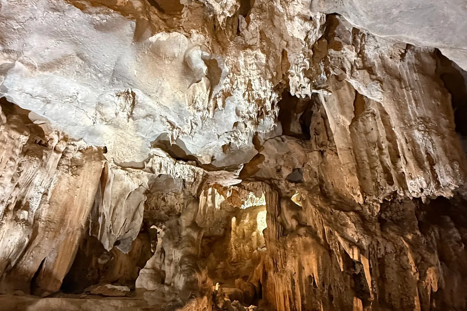 Interior of a limestone cave with stalactites, flowstone walls and a small warm light on the rocky floor.
