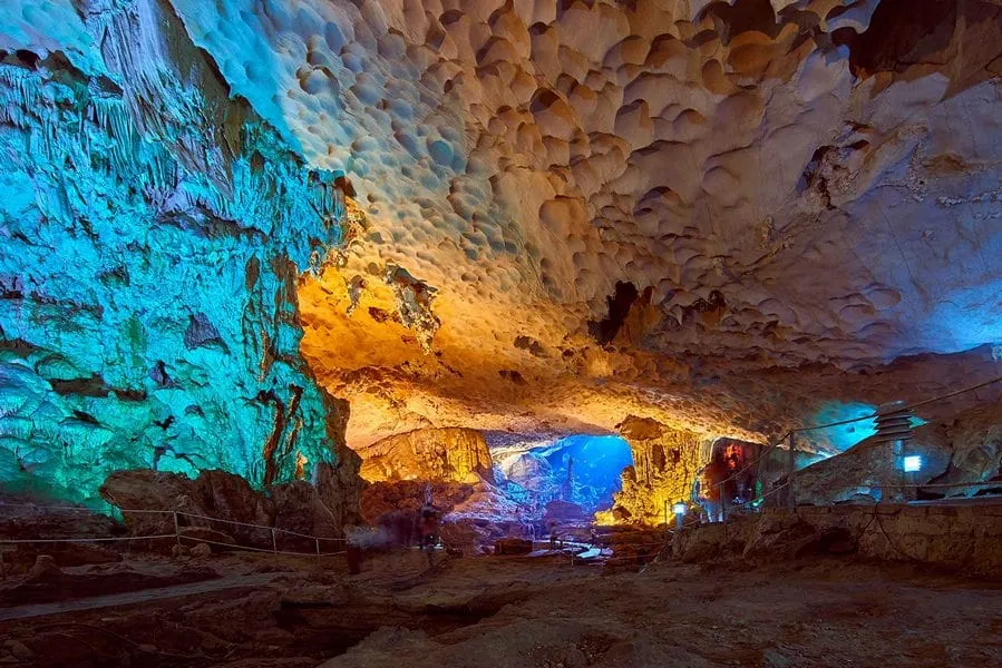 A limestone cave interior with dramatic blue and orange colored lighting illuminating the stalactites and rock formations.
