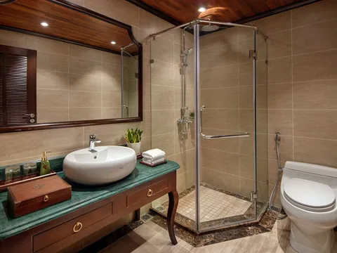A bathroom with beige tiled walls, a glass corner shower, a white toilet, and a dark wood vanity with a green marble top, a white vessel sink, and a large mirror under a wooden ceiling.