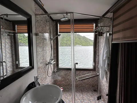 A modern boat bathroom with mosaic tile shower, vessel sink, and window view of green karst islands and water.