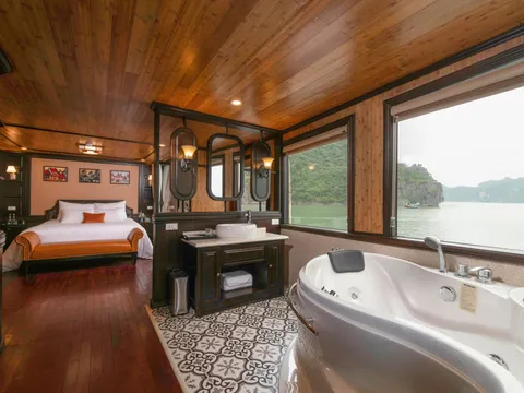 A luxury boat cabin interior with a bed, bathtub, and large windows showing limestone karsts and water outside.