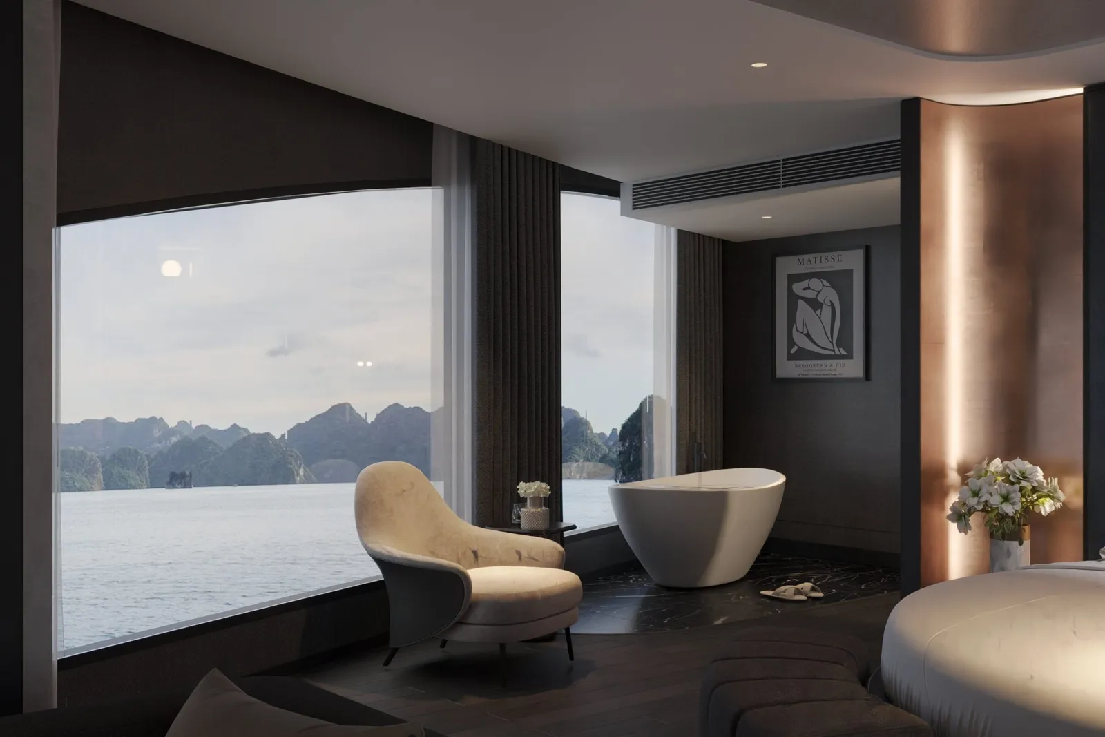 A dark-toned cabin interior with a freestanding white bathtub, cream armchair and round bed, with large windows looking out on limestone karsts over calm water; a framed Matisse poster hangs on the wall.