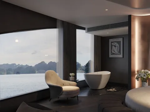 A dark-toned cabin interior with a freestanding white bathtub, cream armchair and round bed, with large windows looking out on limestone karsts over calm water; a framed Matisse poster hangs on the wall.
