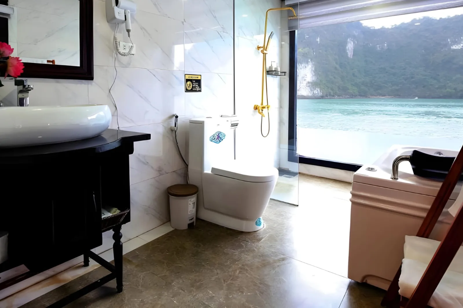 A bathroom with a glass shower, a vessel basin and a window facing the bay.