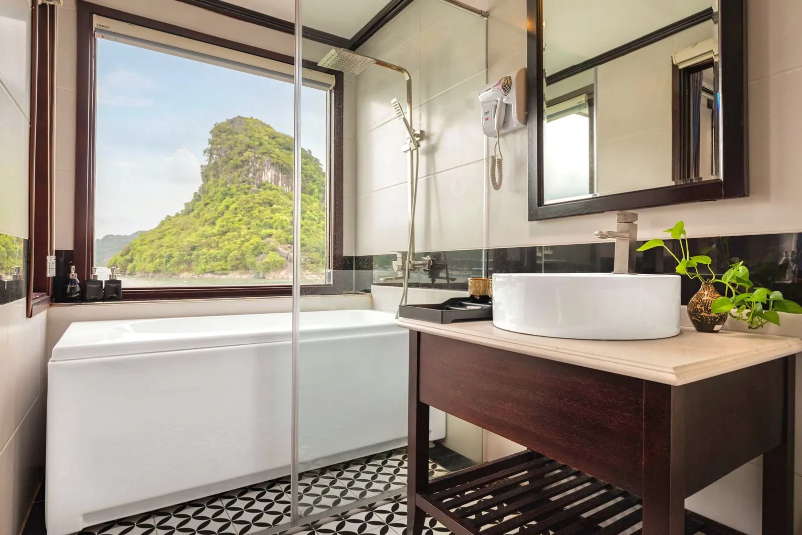 A boat cabin bathroom with a bathtub, sink, and window showing a limestone karst formation outside.