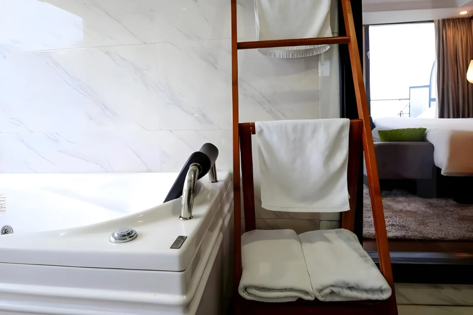 A white bathtub with a towel ladder beside white marble walls.