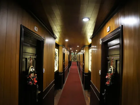 A long interior corridor with wood paneling, black cabin doors decorated with floral ornaments, red carpet runner, and recessed ceiling lights.