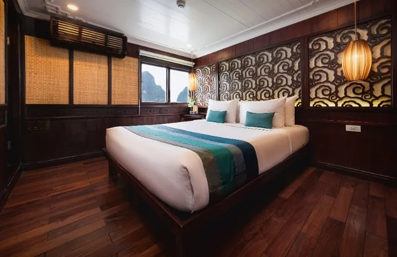 A double cabin with a carved wooden headboard wall, a teal bed runner and a round lantern.