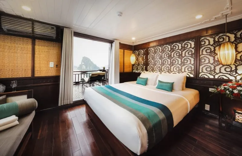 A double cabin with a window and balcony door, teal cushions and a carved wooden headboard.