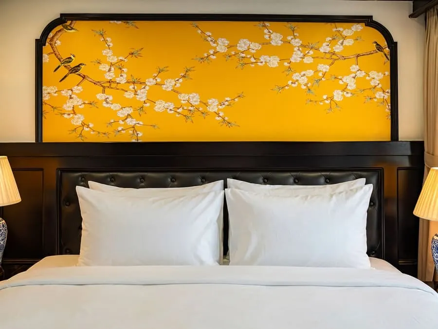 Close view of a bed with white pillows under a yellow floral-painted headboard on dark leather panelling.