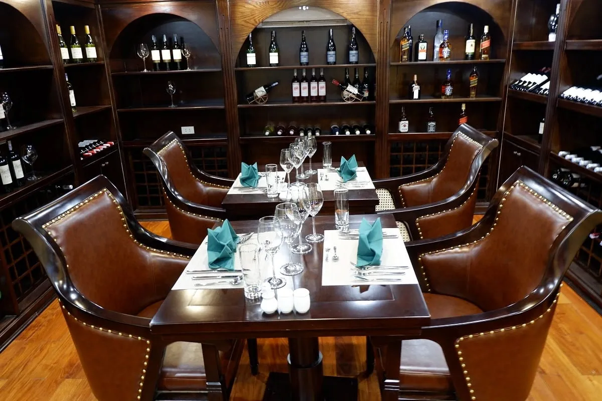 An upscale dining room interior with brown leather chairs, set tables with turquoise napkins, and wooden wine storage shelves covering the walls.