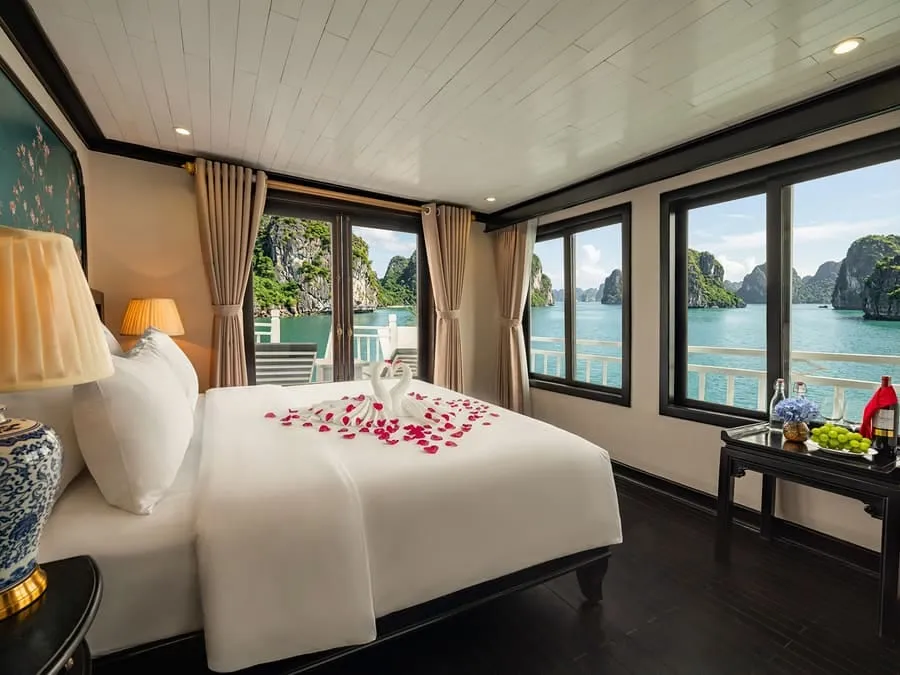 A cabin with a bed set with rose petals and large picture windows looking out at limestone islands.