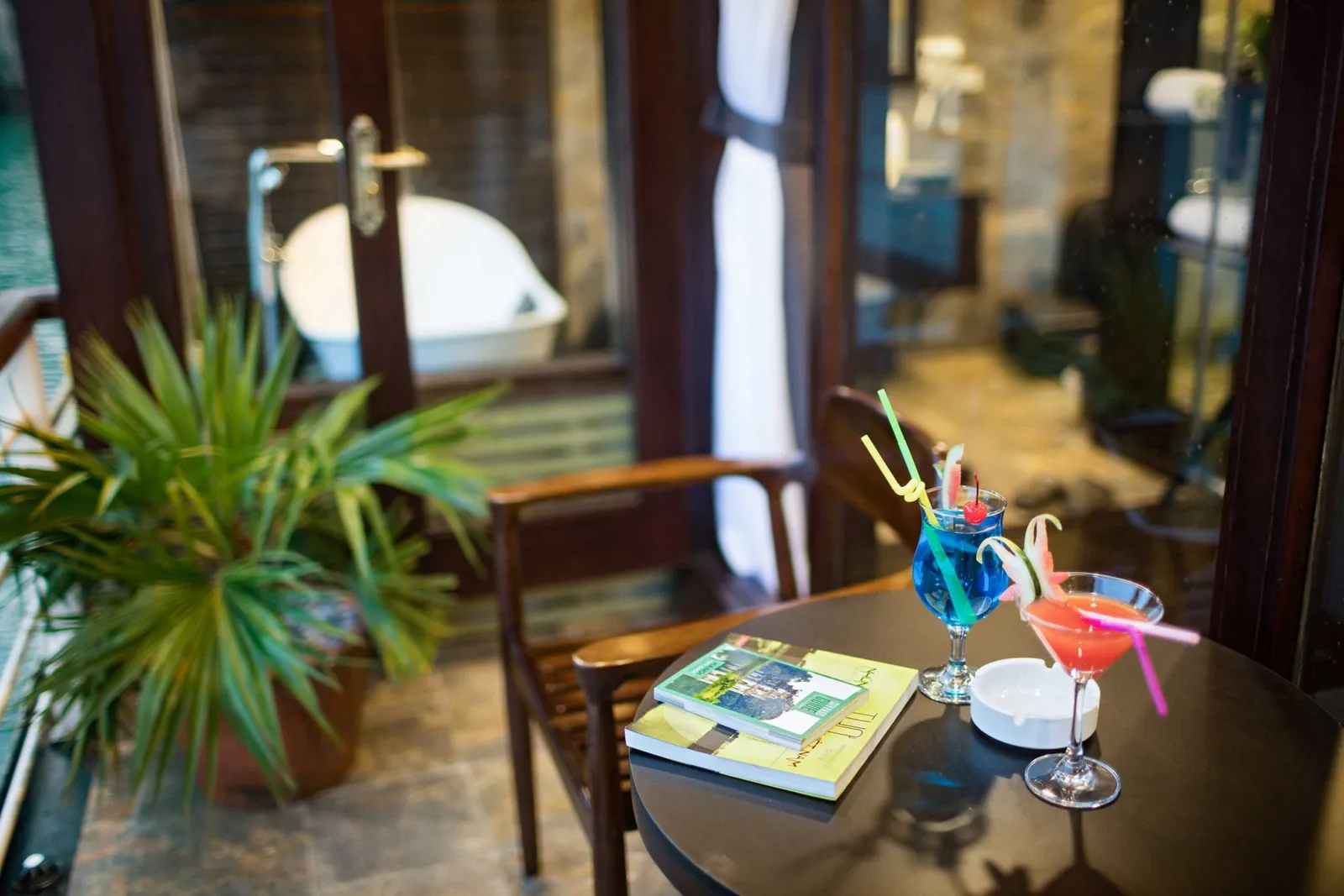 Interior cabin table with cocktails, a book, and a plant, with glass doors showing water view outside.