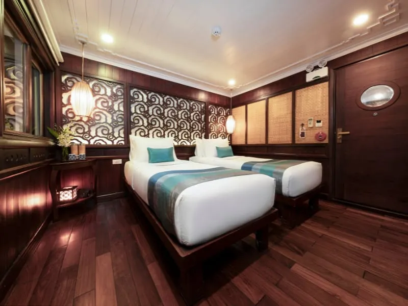 A twin cabin with two beds with teal runners, dark timber floor and carved panelling.