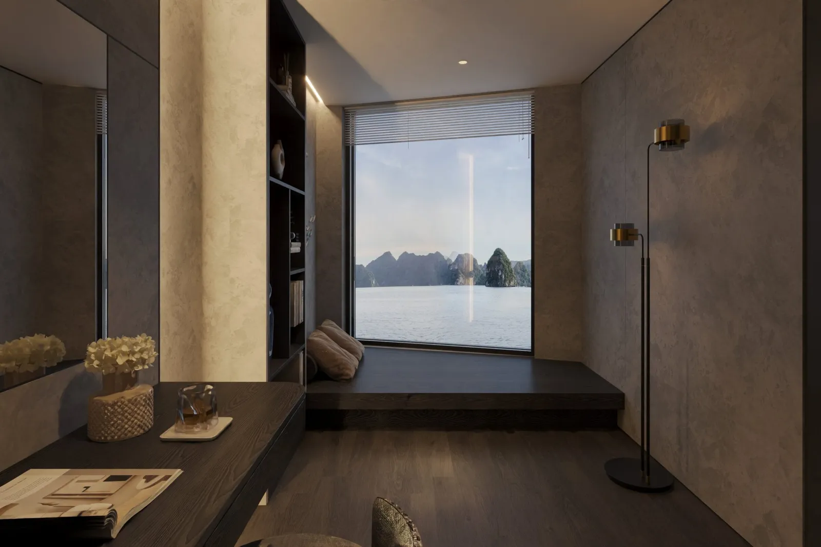 A dark, stone-walled cabin interior with a desk, flowers, a magazine, a floor lamp and a cushioned window seat facing a large window that looks out on calm water and limestone karst islands.