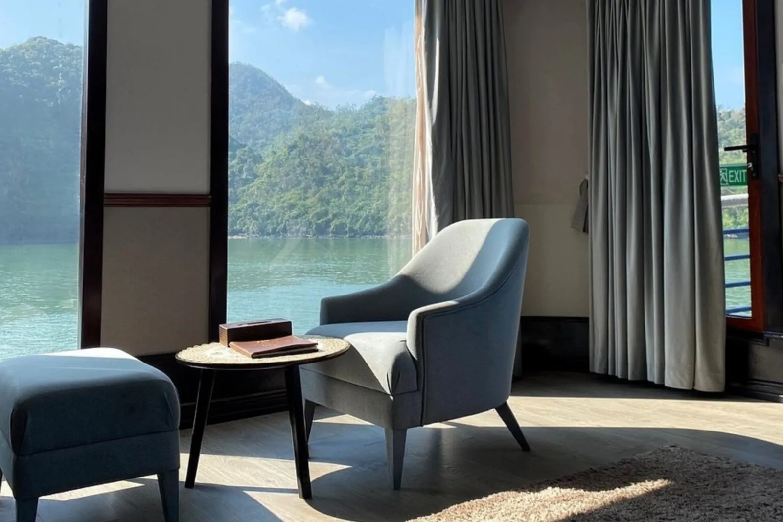 A lounge corner of a cabin with an armchair and footstool by floor-to-ceiling windows.