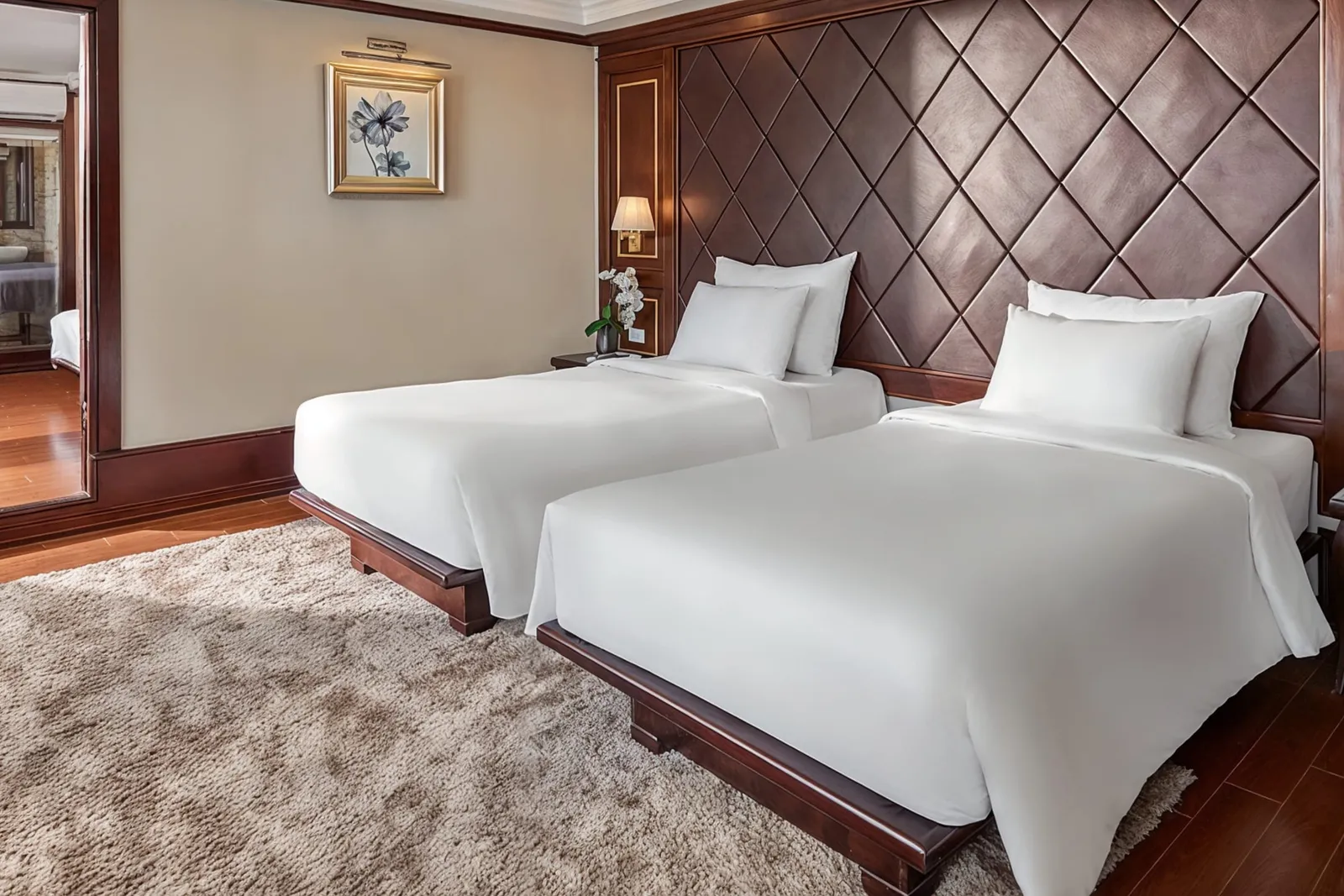 Twin beds with white linen in front of a dark leather diamond headboard wall.