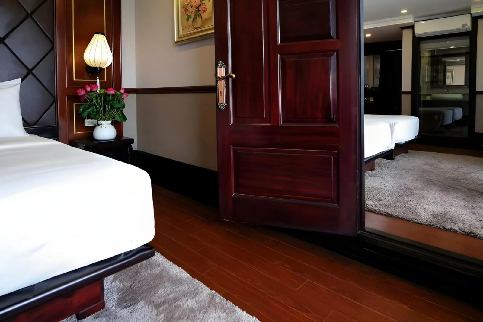 A white bed beside a dark wooden door and framed picture in a cabin.