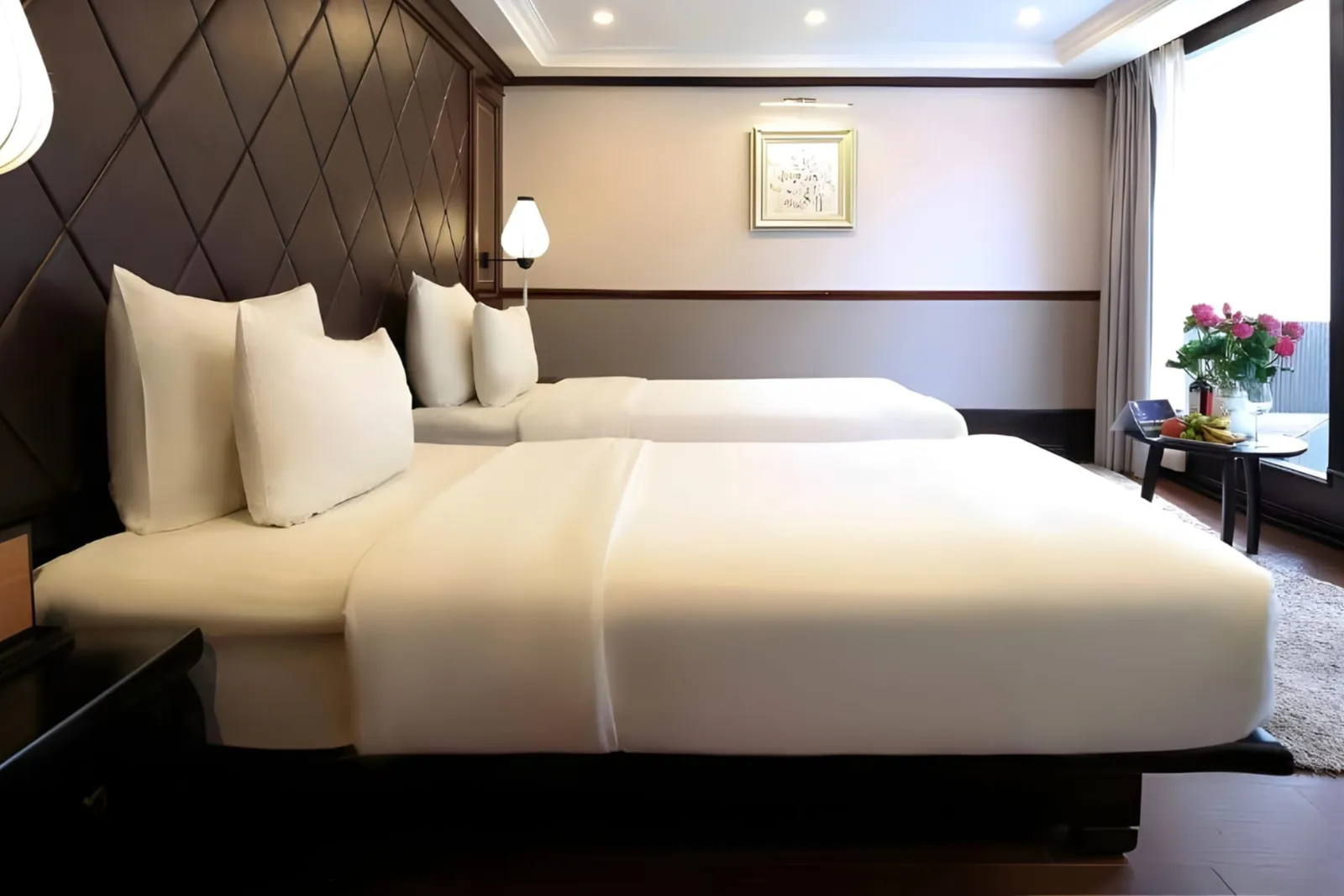 Twin beds in front of a dark diamond-quilted wall with a lantern lamp.