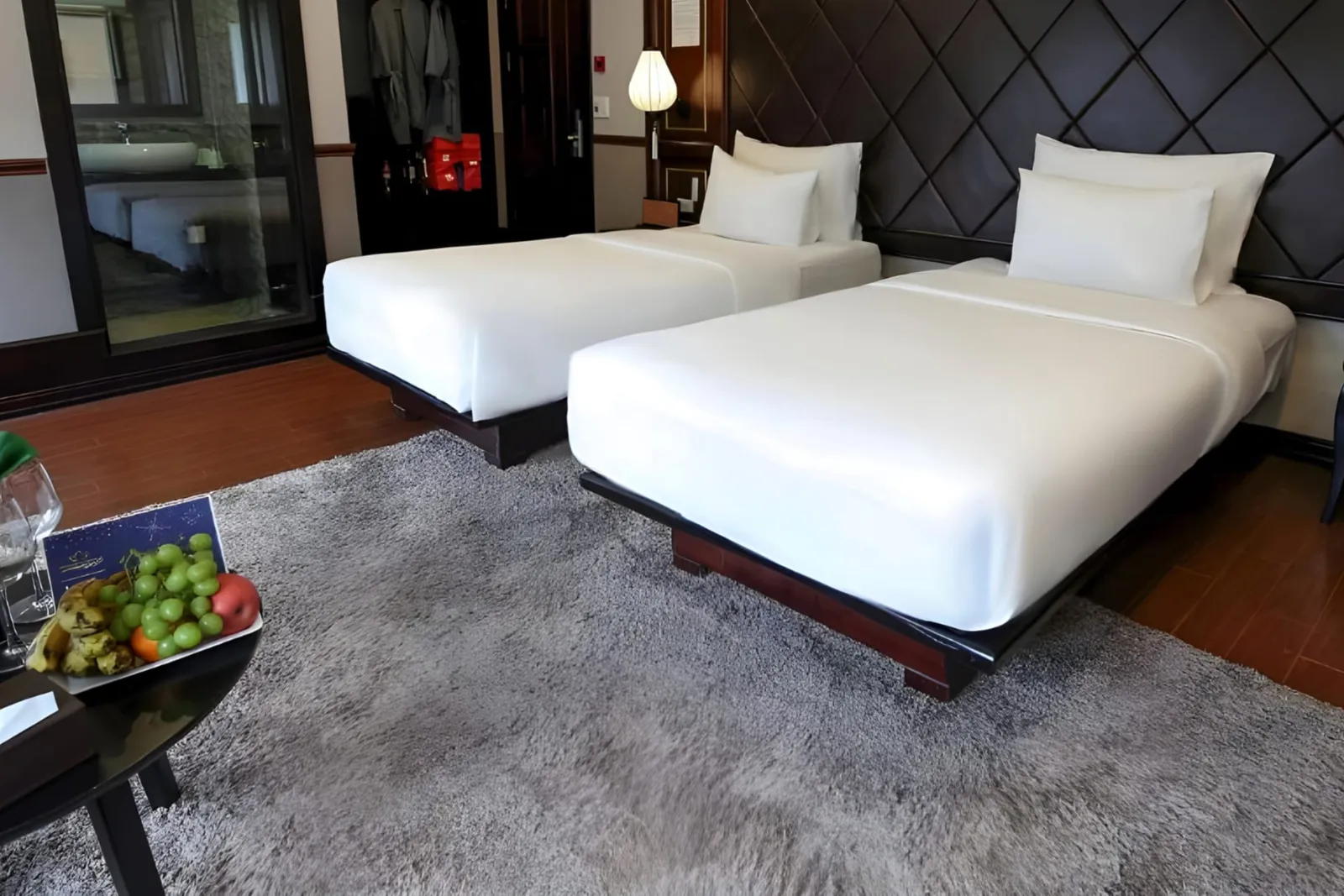 Twin beds with a grey rug and a fruit bowl in a cabin with a diamond-pattern headboard.