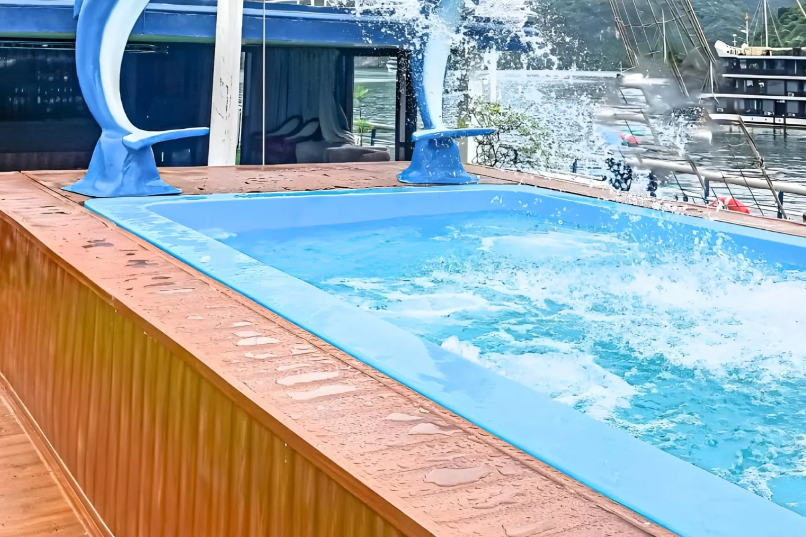 A plunge pool with two blue dolphin statues spouting water on the upper deck, with sail rigging behind.