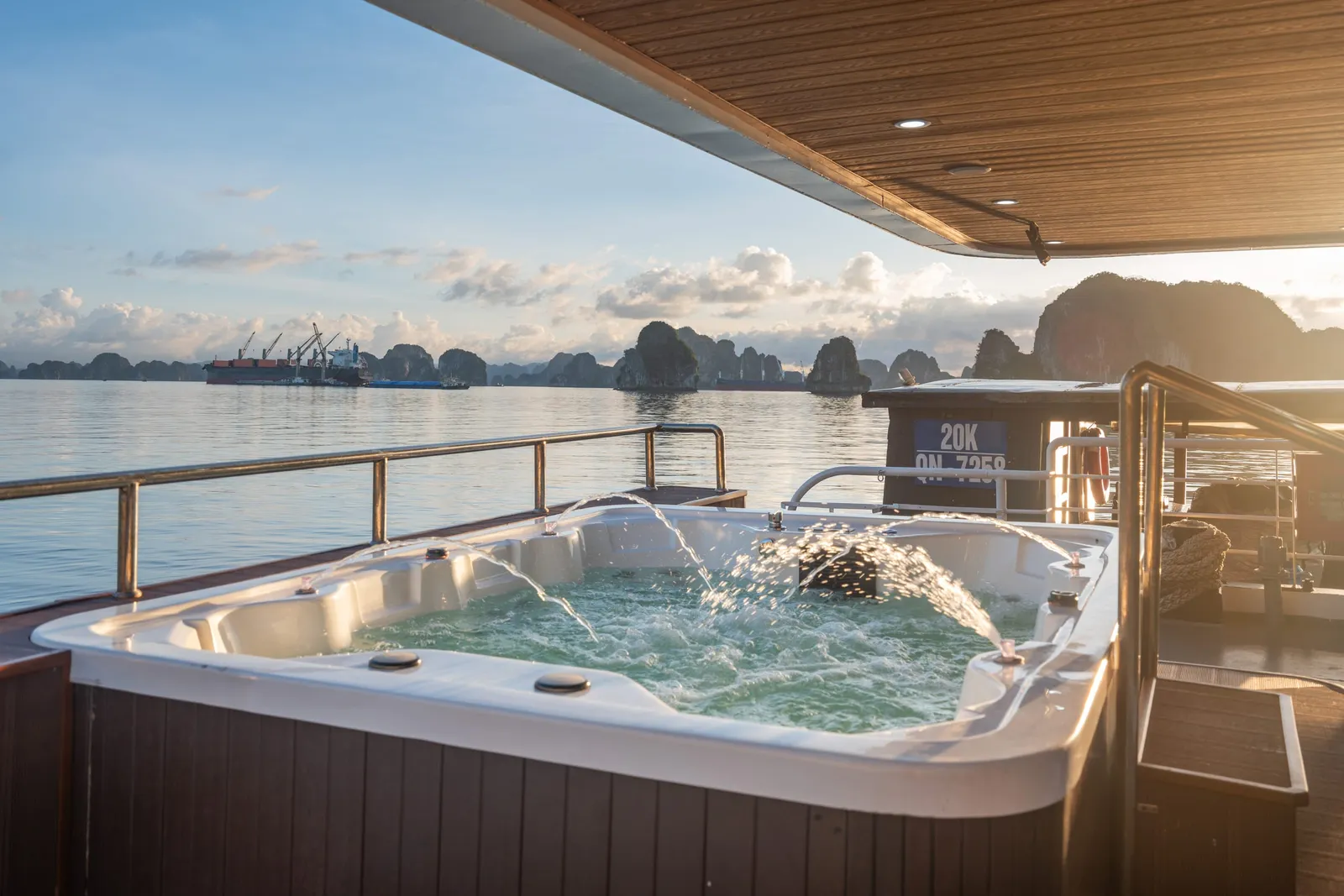 A jacuzzi with water jets on the sundeck, with a wood-panelled railing and a view across the bay to limestone islands.