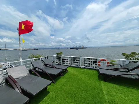 A sun deck with lounge chairs on artificial grass, Vietnamese flag flying, overlooking calm waters with distant limestone karsts and vessels.