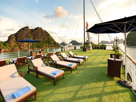 A sun deck with lounge chairs and green artificial turf on a cruise boat with limestone karsts in the background.