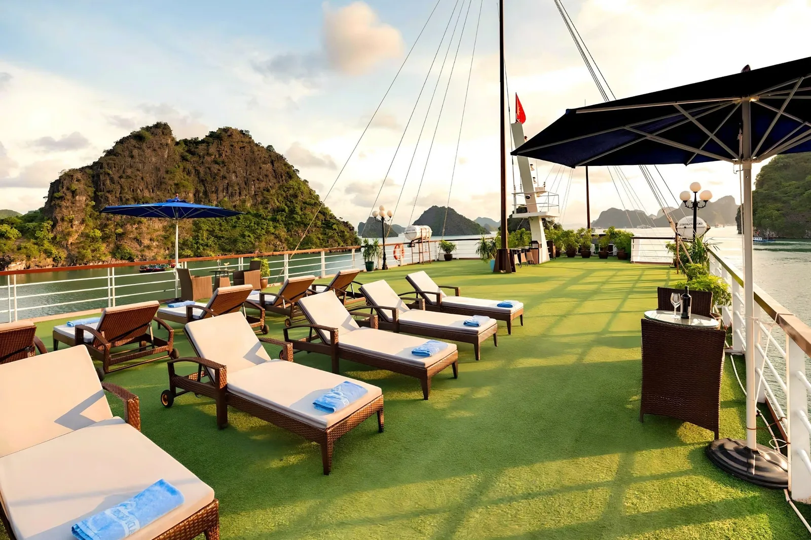 A sun deck with lounge chairs and green artificial turf on a cruise boat with limestone karsts in the background.