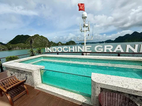 A swimming pool on a boat deck with large three-dimensional letters spelling INDOCHINE GRAN mounted on the railing, with limestone karsts and water in the background.