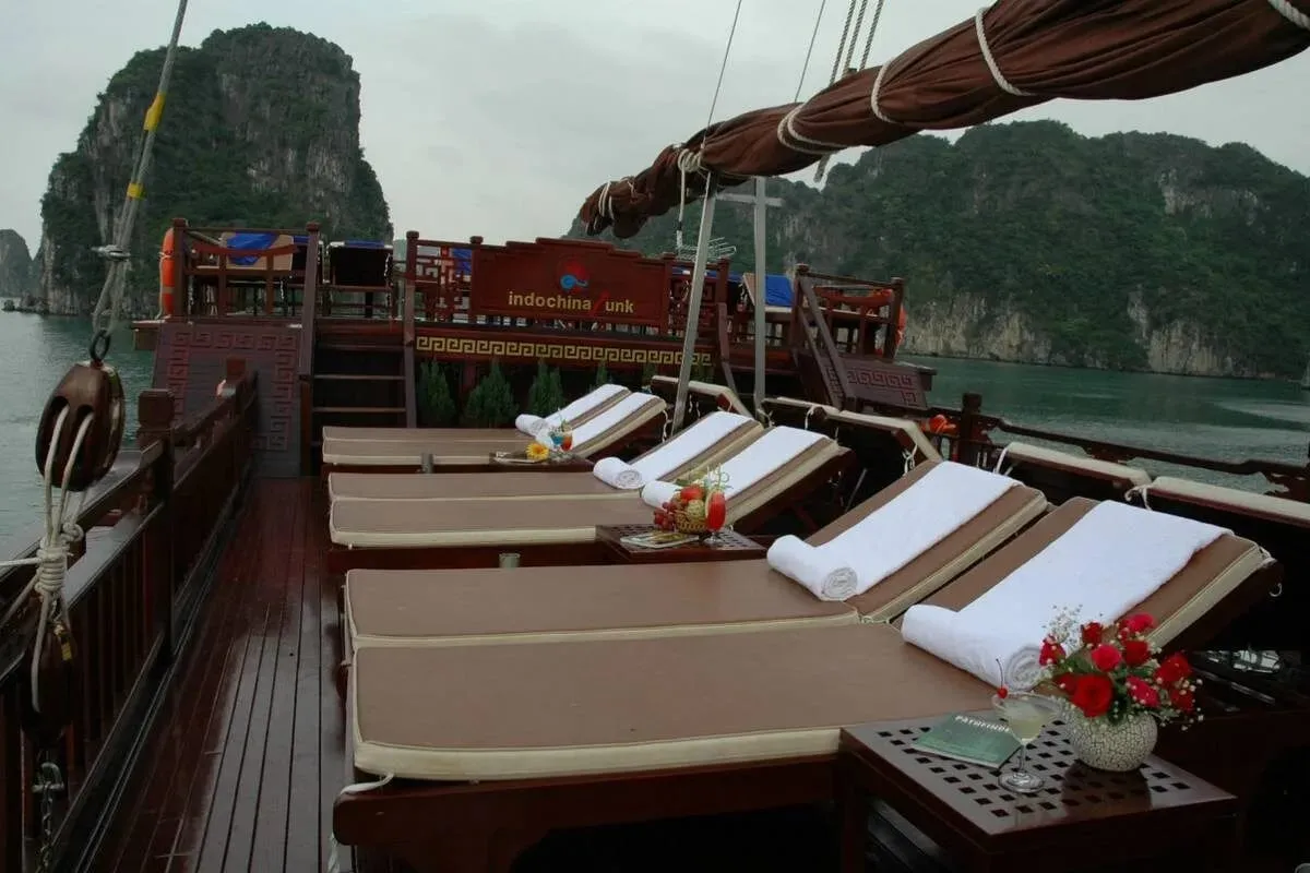 Sun loungers with white towels beside a dark timber rail and a flower arrangement.