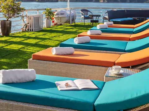 Orange and teal sun loungers on the green-turf sundeck with limestone islands across the water.