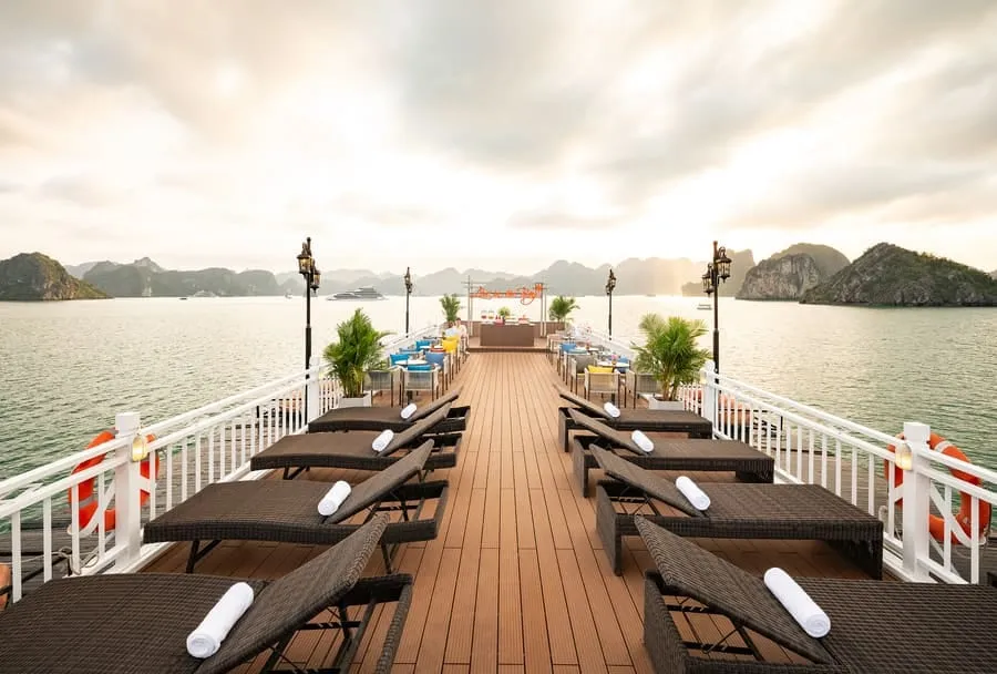 Rows of dark wooden sun loungers with white towels on both sides of the timber sundeck.