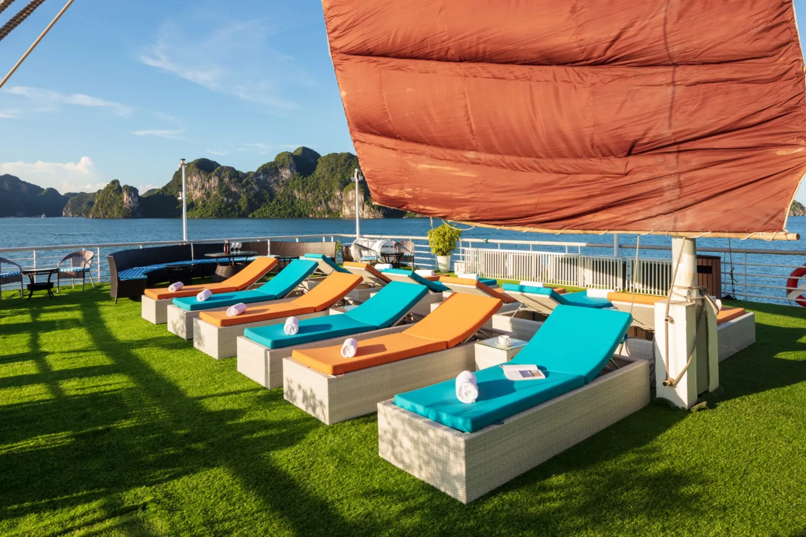An orange sail above a row of loungers on the turf sundeck, with a lifebuoy at the rail.