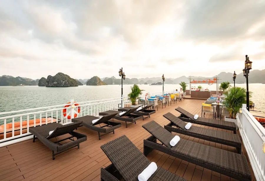 Sun loungers along the railing of the timber sundeck with a lifebuoy and a hazy bay behind.
