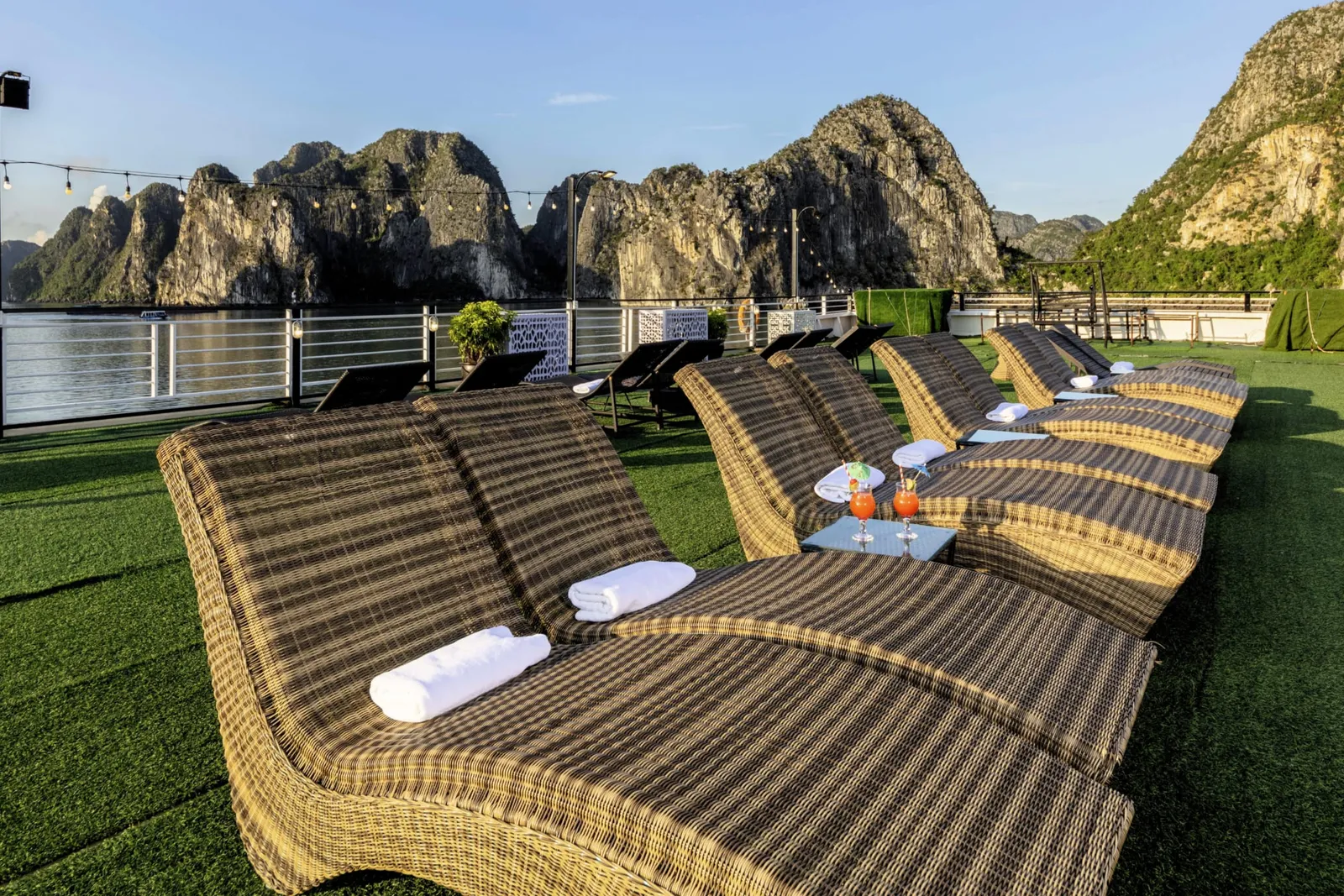 Rattan loungers with white towels on the green turf deck with a karst ridge behind.