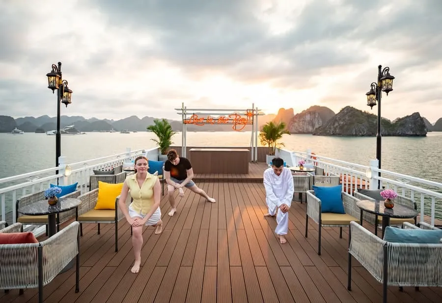 Guests stretching on the timber sundeck among wicker chairs, with the neon Live in the Bay sign behind.