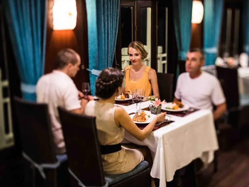 Guests dining at a white-clothed table with teal curtains behind.
