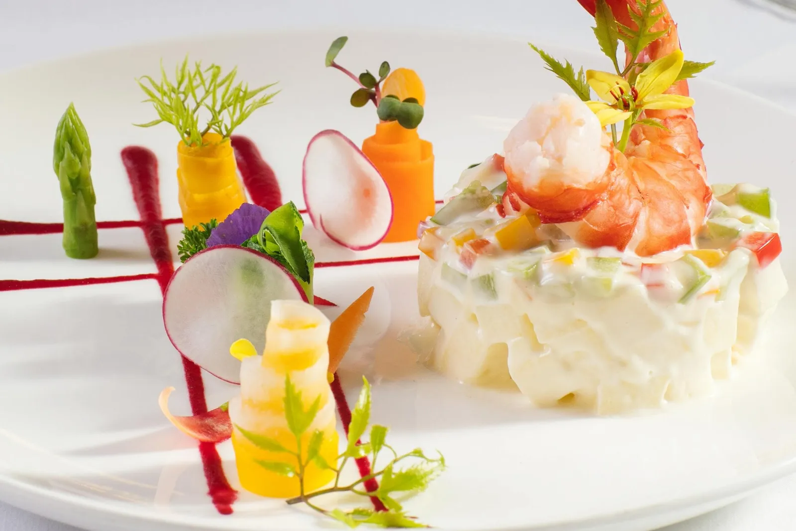 An artfully plated appetizer with shrimp, vegetable garnishes, and decorative carved vegetables on a white square plate.