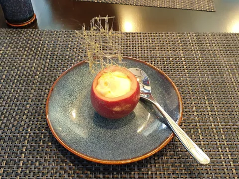 A plated dessert served in a hollowed tomato with a decorative garnish on a woven placemat at a dining table.