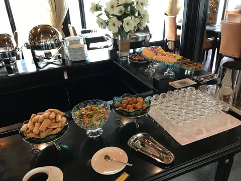 A buffet table with pastries, salads, and serving dishes set up in a dining room with large windows and curtains.