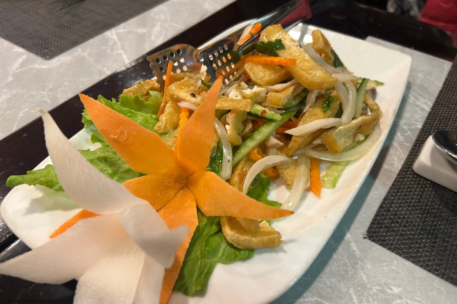 A plated salad dish with fried items, vegetables, and decorative carrot garnish on a dining table.
