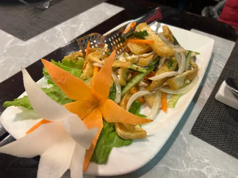 A plated salad dish with fried items, vegetables, and decorative carrot garnish on a dining table.